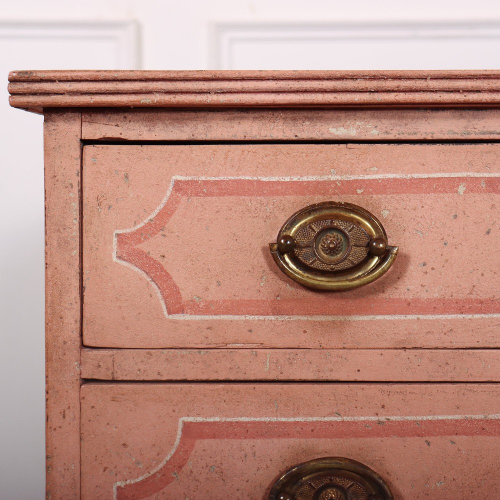 An antique English four-drawer chest featuring a muted pink painted finish with contrasting painted frame borders and brass oval handles on bracket feet. View VII