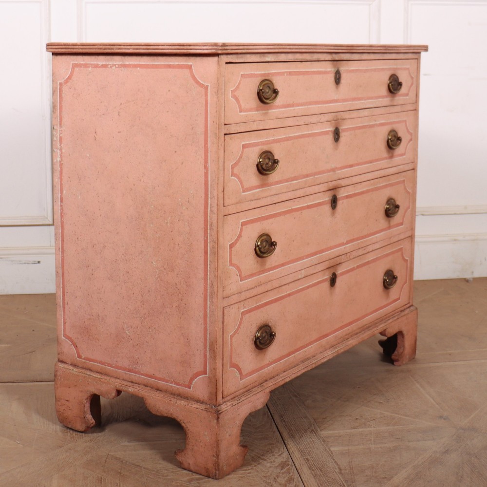 An antique English four-drawer chest featuring a muted pink painted finish with contrasting painted frame borders and brass oval handles on bracket feet. View VIII