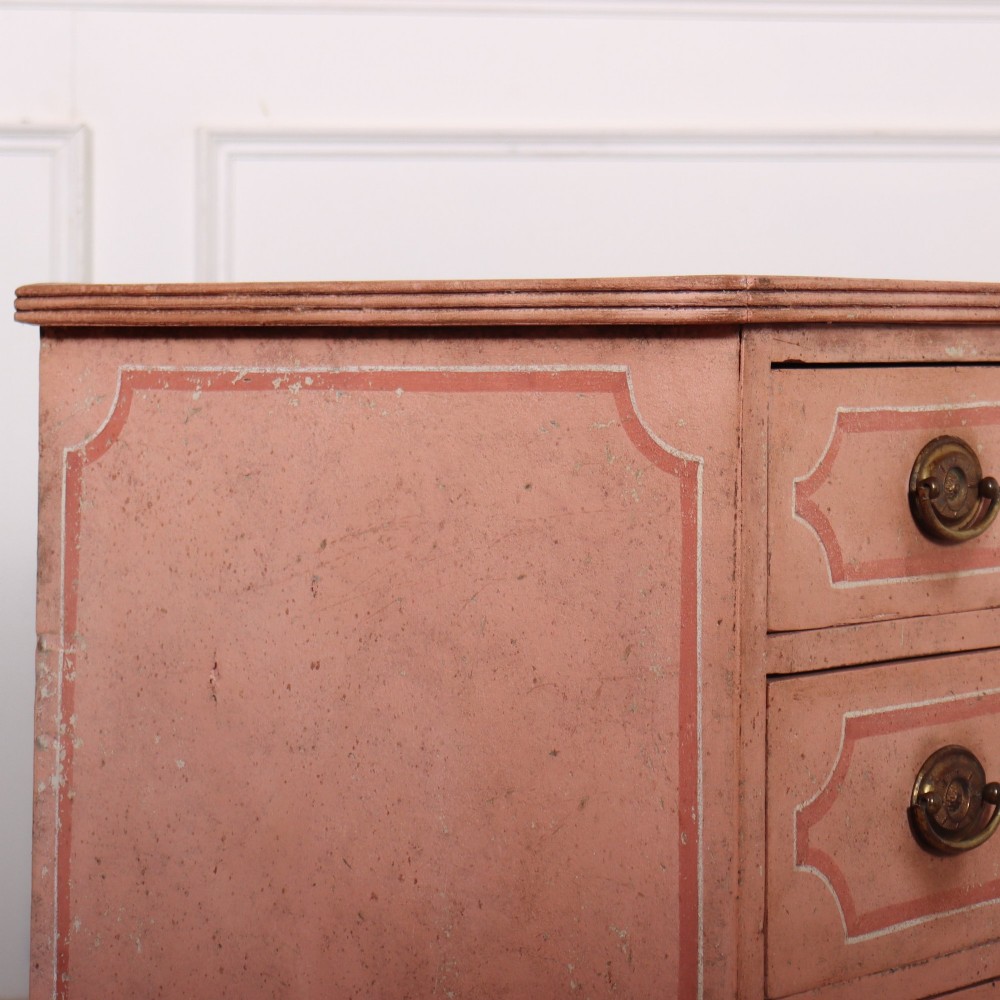 An antique English four-drawer chest featuring a muted pink painted finish with contrasting painted frame borders and brass oval handles on bracket feet. View IX