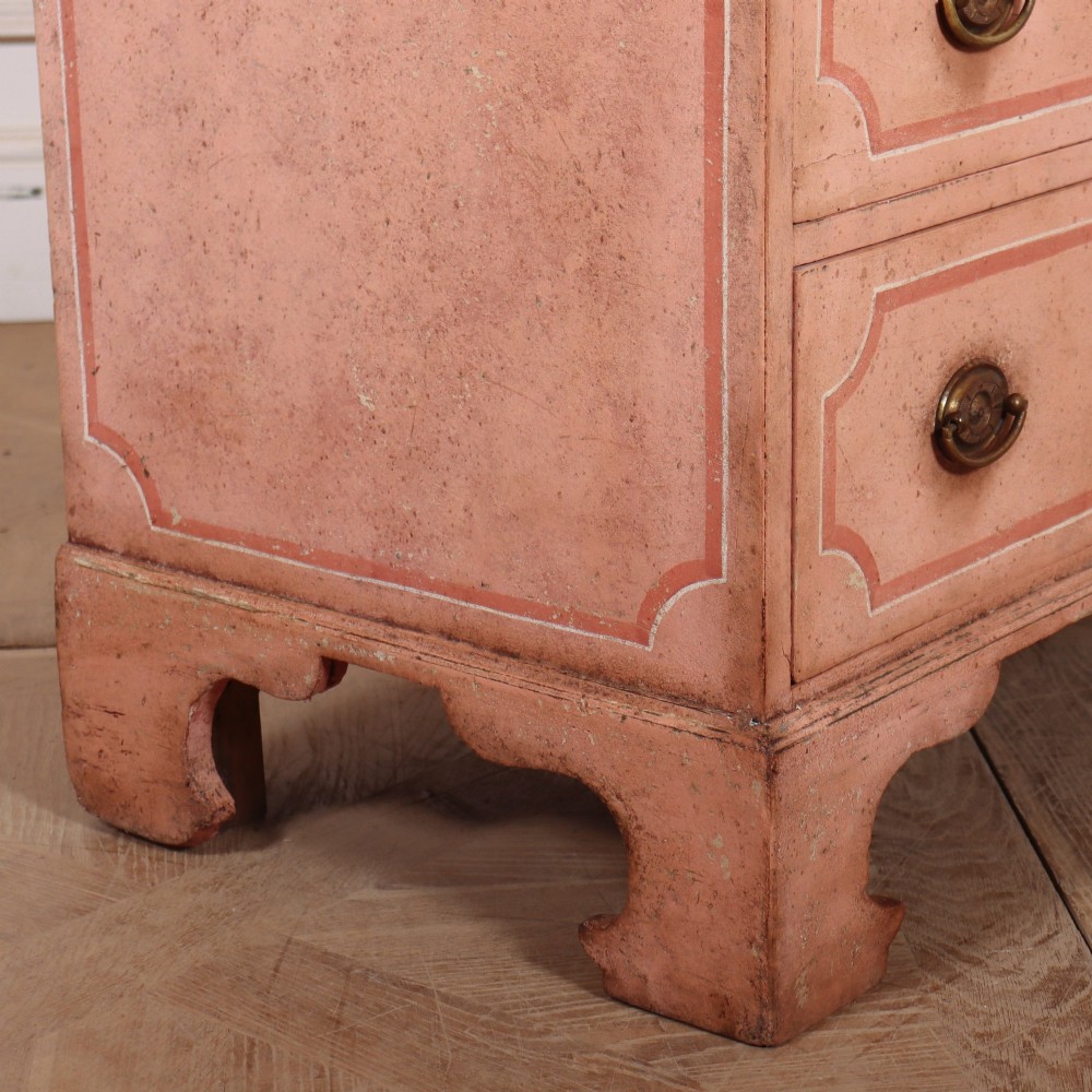 An antique English four-drawer chest featuring a muted pink painted finish with contrasting painted frame borders and brass oval handles on bracket feet. View X