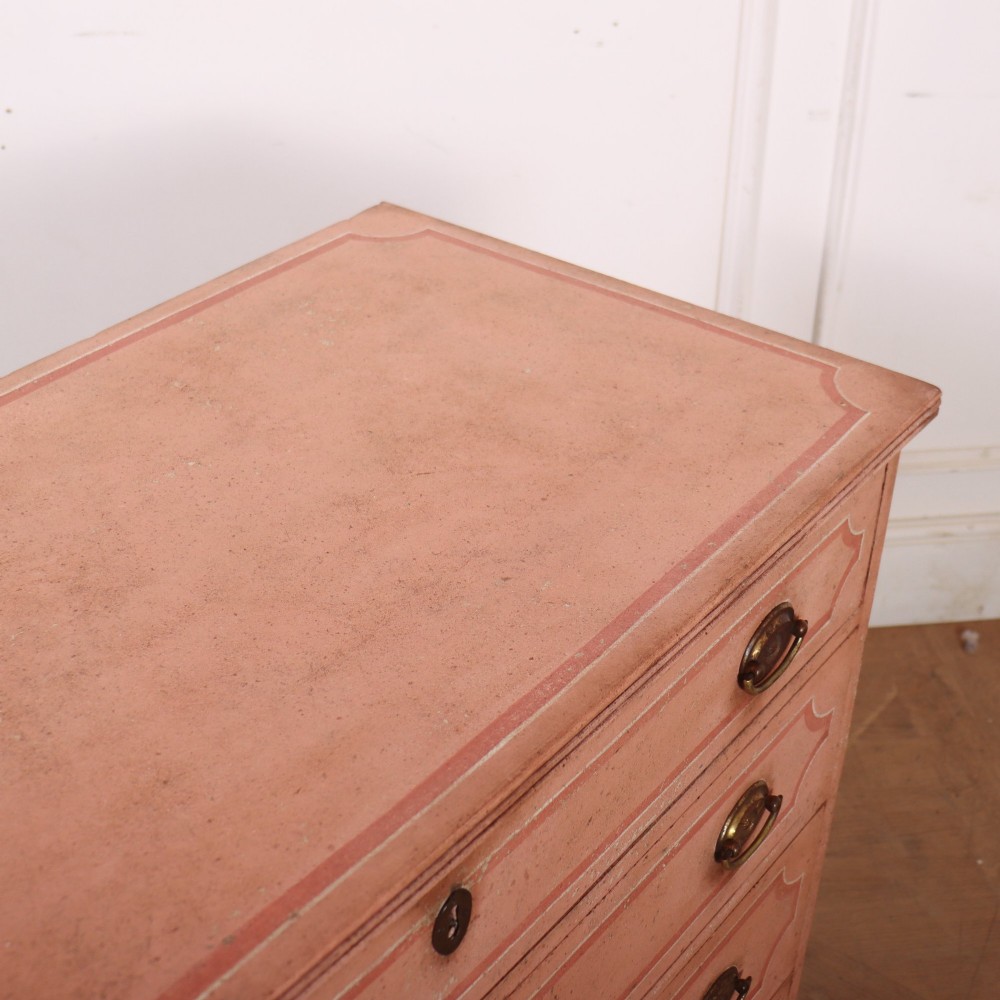 An antique English four-drawer chest featuring a muted pink painted finish with contrasting painted frame borders and brass oval handles on bracket feet. View XII