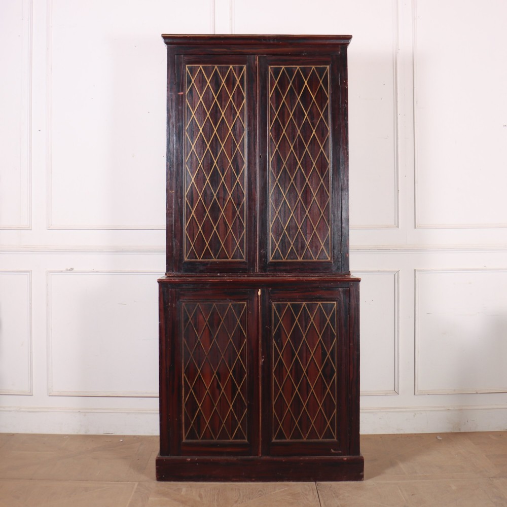 A tall 19th-century dark painted wooden cupboard with two tiers of double doors decorated with gold painted diamond lattice panels.