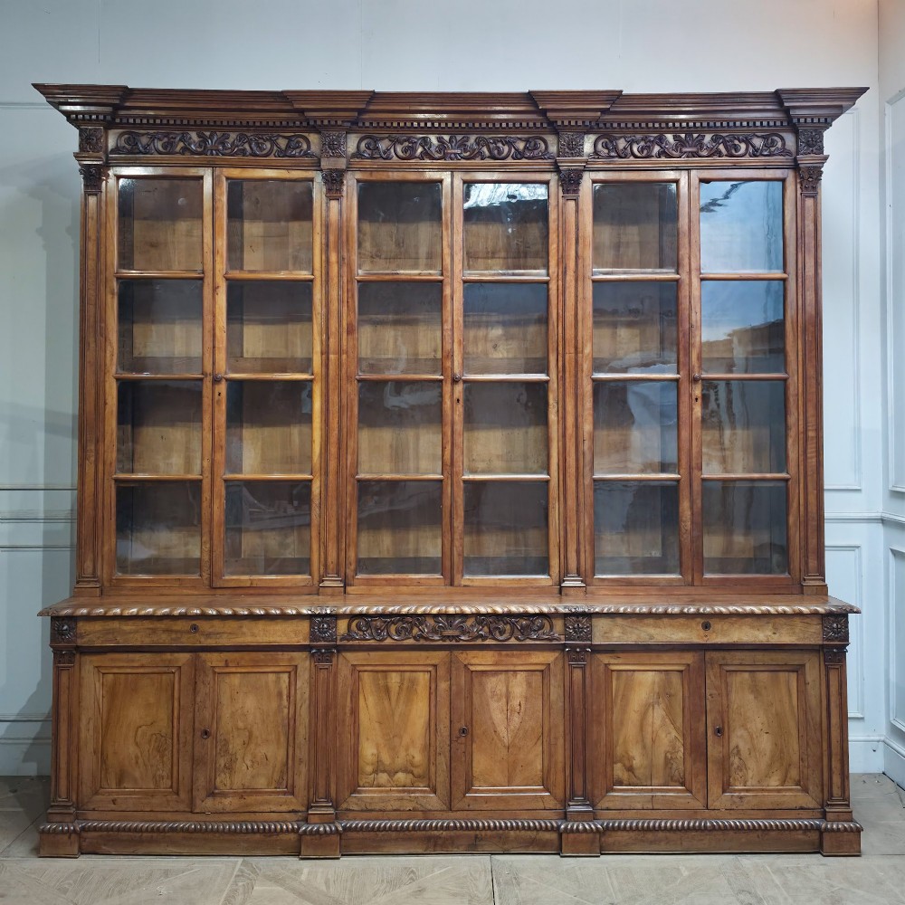 A large French walnut bookcase featuring six glazed upper doors above six panelled lower cupboard doors with carved scrollwork along the upper frieze.