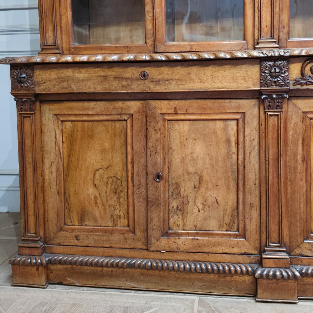 A large French walnut bookcase featuring six glazed upper doors above six panelled lower cupboard doors with carved scrollwork along the upper frieze. View II