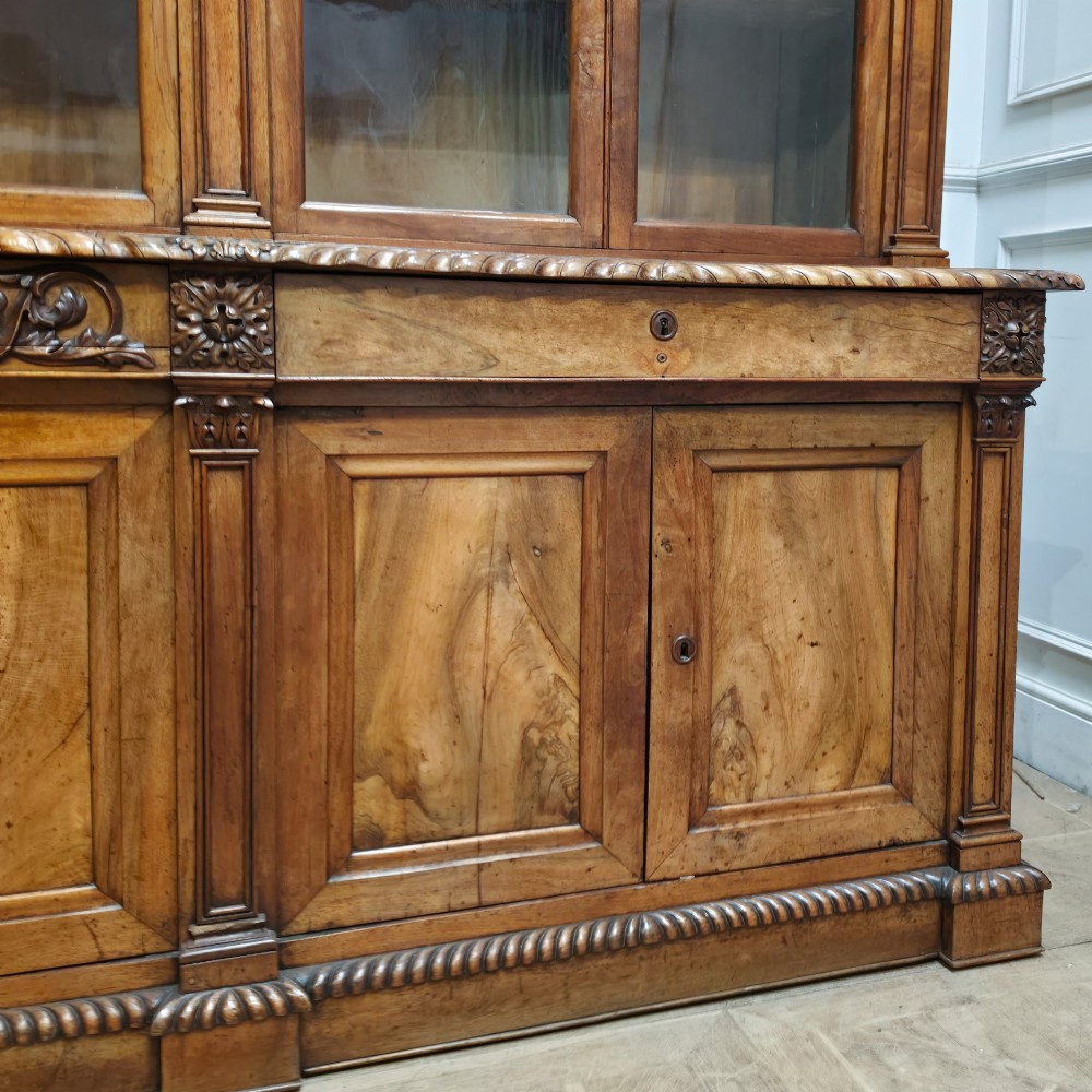 A large French walnut bookcase featuring six glazed upper doors above six panelled lower cupboard doors with carved scrollwork along the upper frieze. View IV