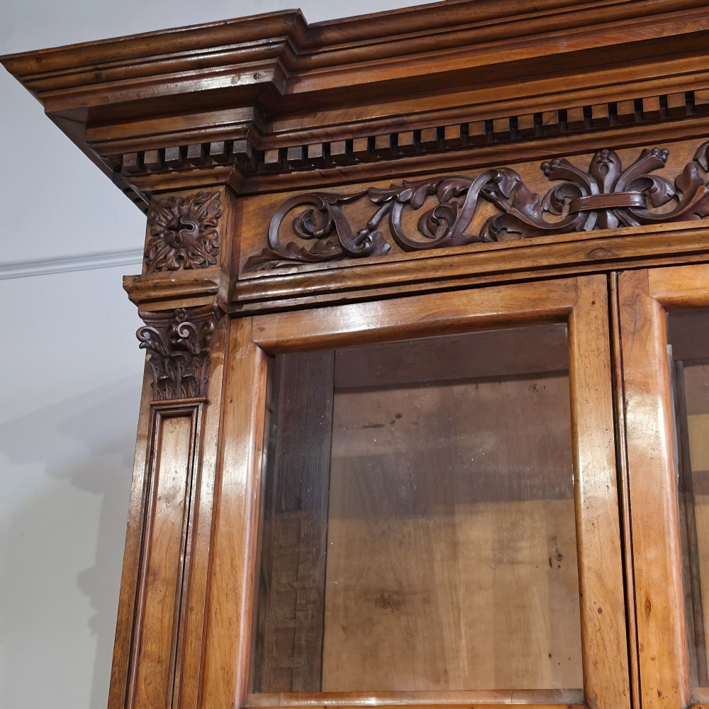 A large French walnut bookcase featuring six glazed upper doors above six panelled lower cupboard doors with carved scrollwork along the upper frieze. View V