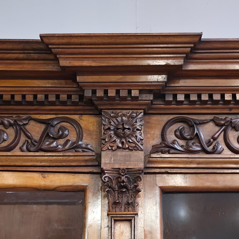 A large French walnut bookcase featuring six glazed upper doors above six panelled lower cupboard doors with carved scrollwork along the upper frieze. View VI