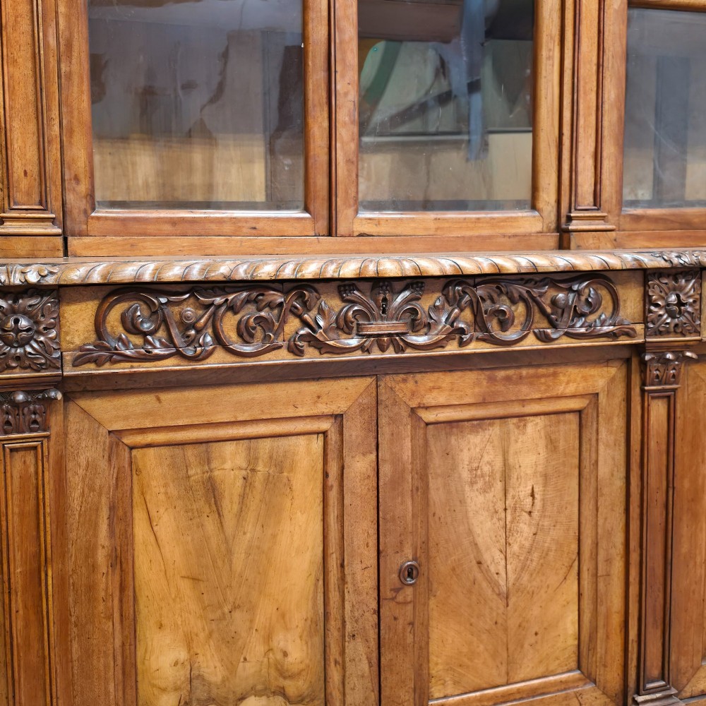 A large French walnut bookcase featuring six glazed upper doors above six panelled lower cupboard doors with carved scrollwork along the upper frieze. View VIII