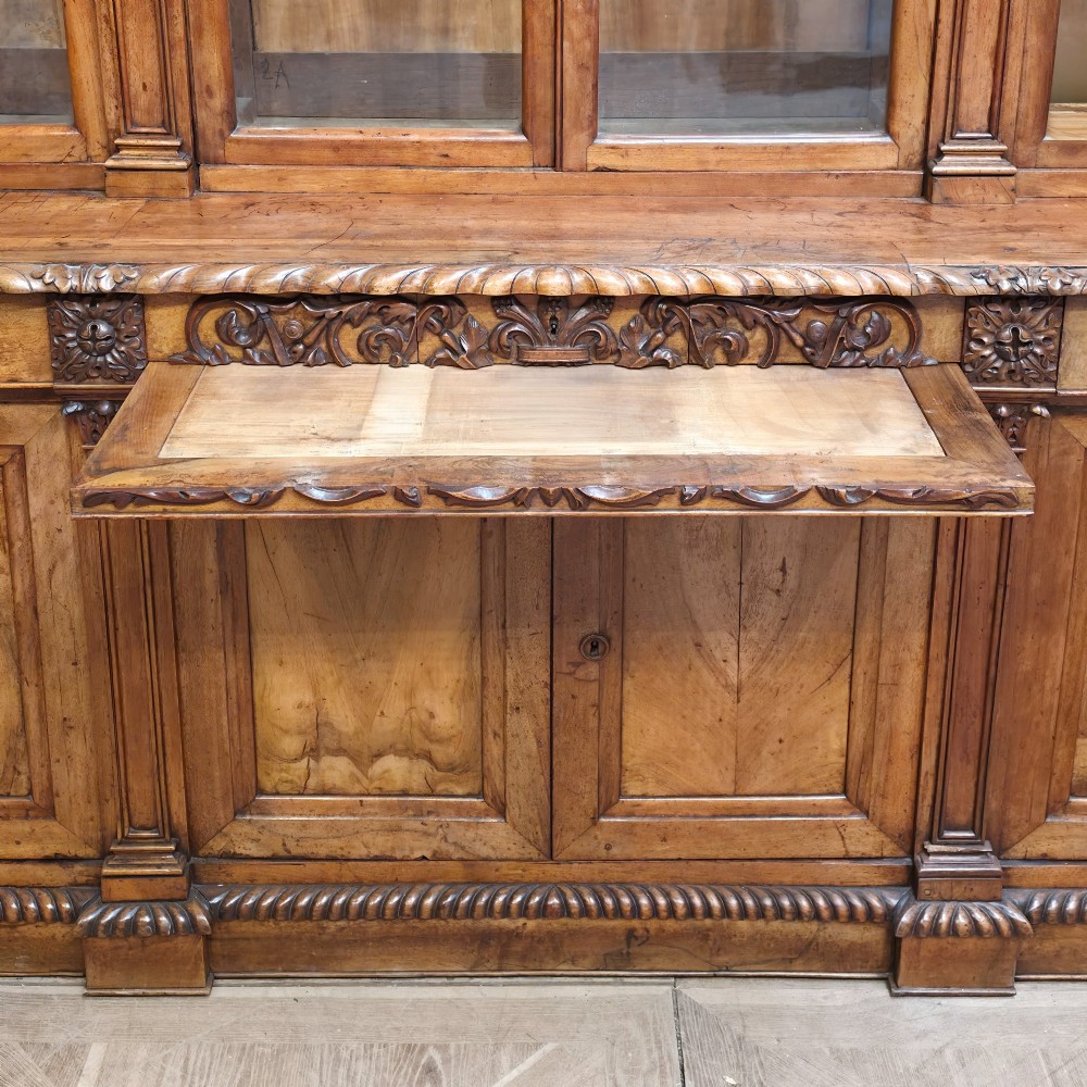 A large French walnut bookcase featuring six glazed upper doors above six panelled lower cupboard doors with carved scrollwork along the upper frieze. View XI