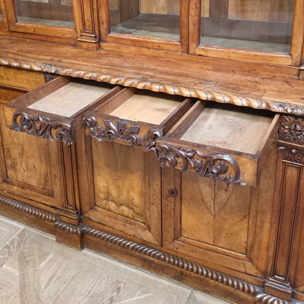 A large French walnut bookcase featuring six glazed upper doors above six panelled lower cupboard doors with carved scrollwork along the upper frieze. View XII