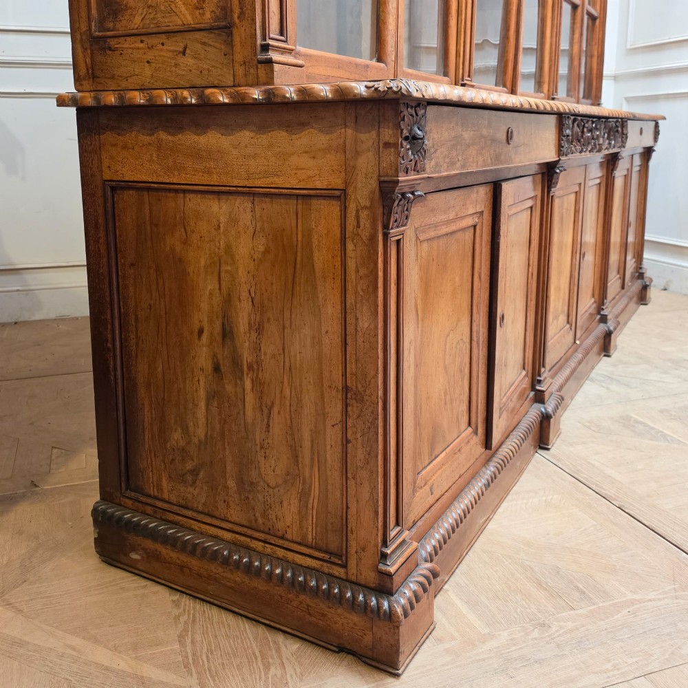 A large French walnut bookcase featuring six glazed upper doors above six panelled lower cupboard doors with carved scrollwork along the upper frieze. View XIV