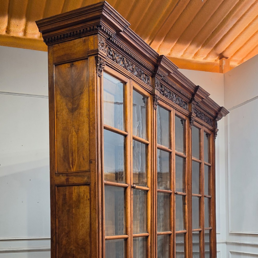 A large French walnut bookcase featuring six glazed upper doors above six panelled lower cupboard doors with carved scrollwork along the upper frieze. View XV