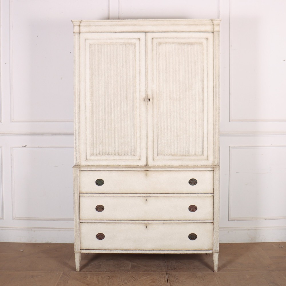 A tall off-white painted Scandinavian style linen cupboard featuring a two-door upper section above three drawers with circular brass handles.