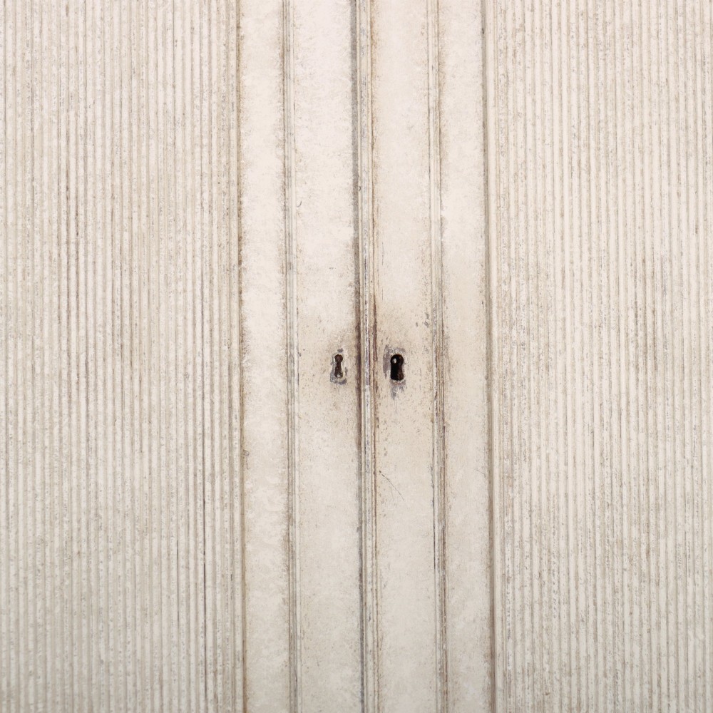 A tall off-white painted Scandinavian style linen cupboard featuring a two-door upper section above three drawers with circular brass handles. View IV
