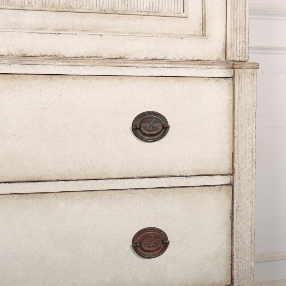 A tall off-white painted Scandinavian style linen cupboard featuring a two-door upper section above three drawers with circular brass handles. View VI