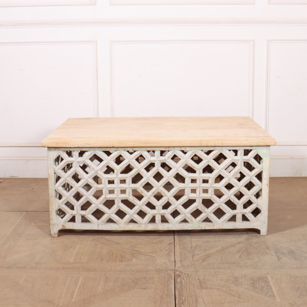 A low rectangular coffee table featuring a plain natural wood top supported by a whitewashed base with geometric lattice fretwork.