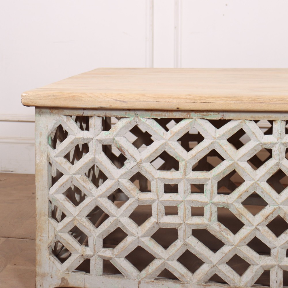 A low rectangular coffee table featuring a plain natural wood top supported by a whitewashed base with geometric lattice fretwork. View II