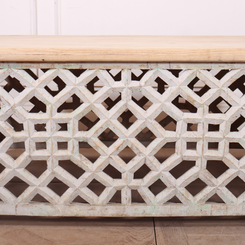 A low rectangular coffee table featuring a plain natural wood top supported by a whitewashed base with geometric lattice fretwork. View VI