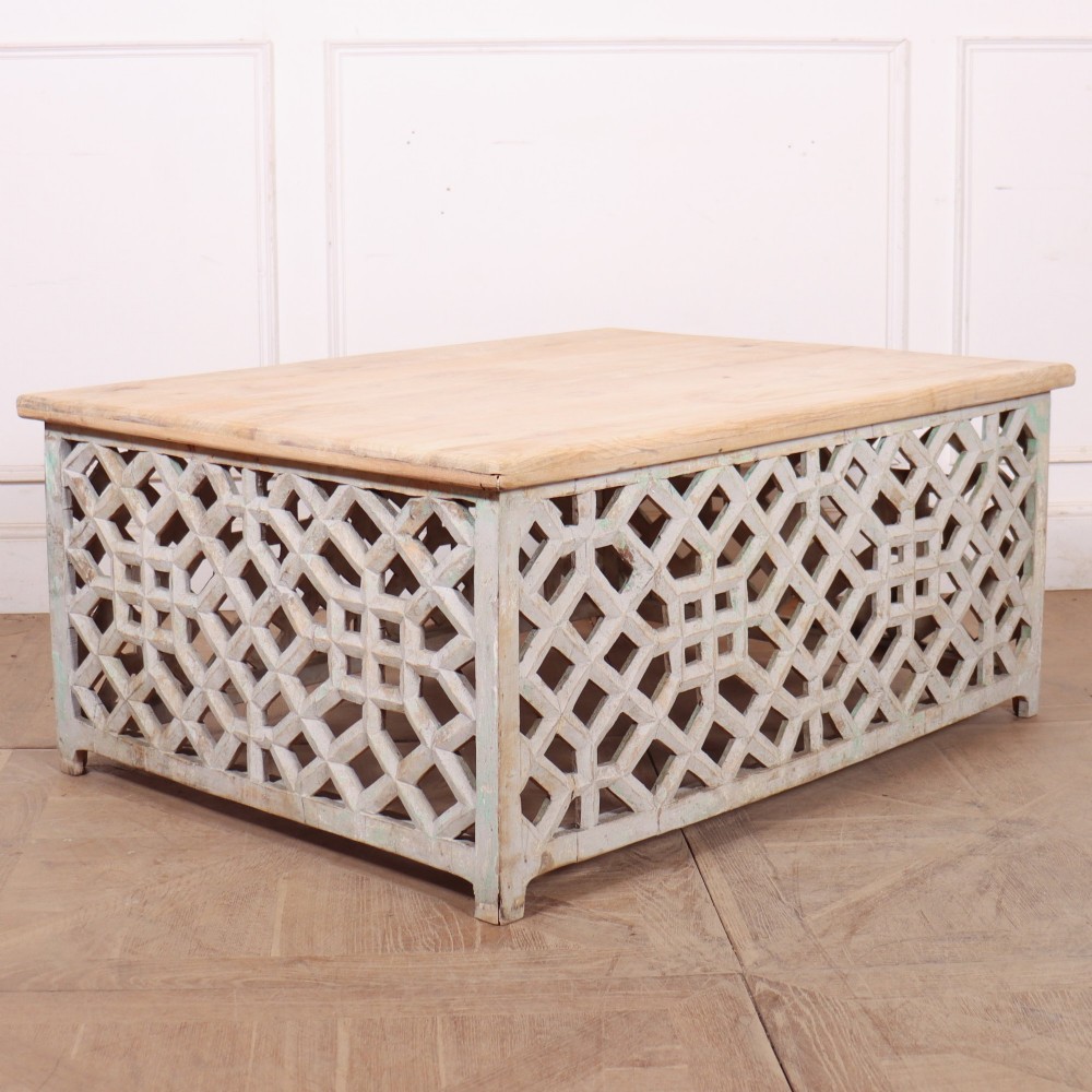 A low rectangular coffee table featuring a plain natural wood top supported by a whitewashed base with geometric lattice fretwork. View VII