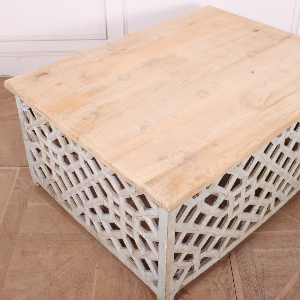 A low rectangular coffee table featuring a plain natural wood top supported by a whitewashed base with geometric lattice fretwork. View VIII