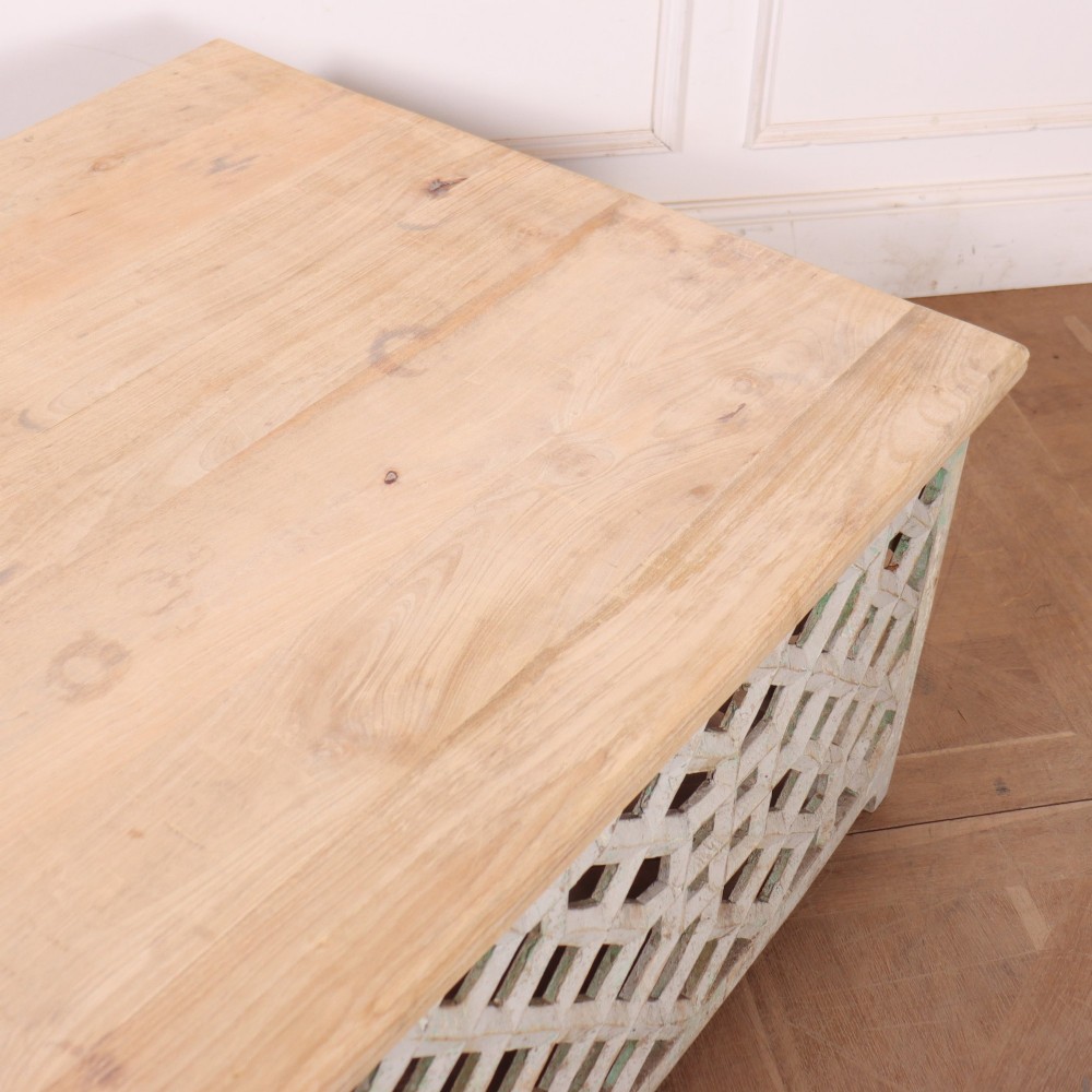 A low rectangular coffee table featuring a plain natural wood top supported by a whitewashed base with geometric lattice fretwork. View IX