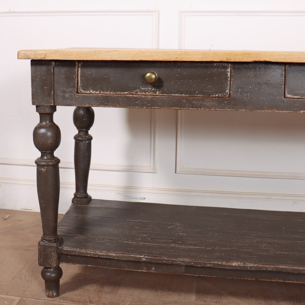 A French drapers table featuring a natural wood top, two shallow drawers with brass knobs, a dark grey painted base, turned legs, and a lower pot board shelf. View II