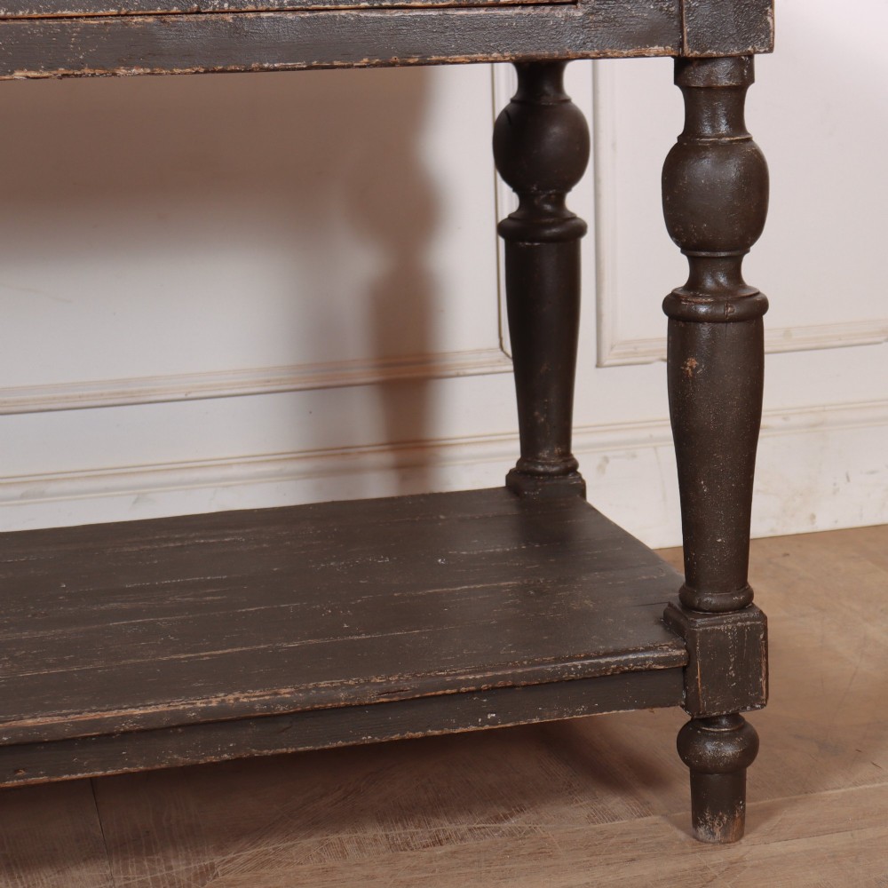 A French drapers table featuring a natural wood top, two shallow drawers with brass knobs, a dark grey painted base, turned legs, and a lower pot board shelf. View V