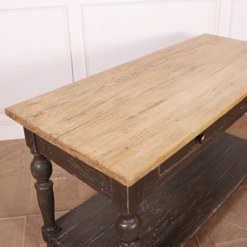 A French drapers table featuring a natural wood top, two shallow drawers with brass knobs, a dark grey painted base, turned legs, and a lower pot board shelf. View VIII