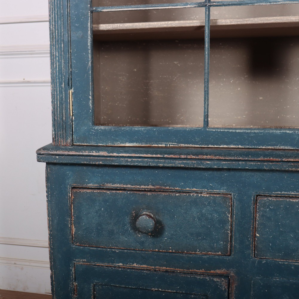A blue-painted two-part timber dresser featuring an upper section with two glazed six-pane doors and a lower base with three drawers above three panelled cupboard doors. View IV