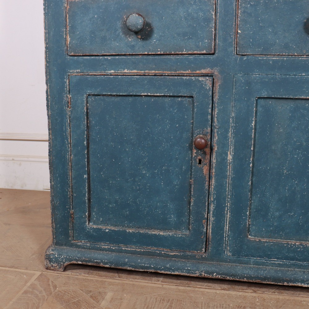 A blue-painted two-part timber dresser featuring an upper section with two glazed six-pane doors and a lower base with three drawers above three panelled cupboard doors. View VI