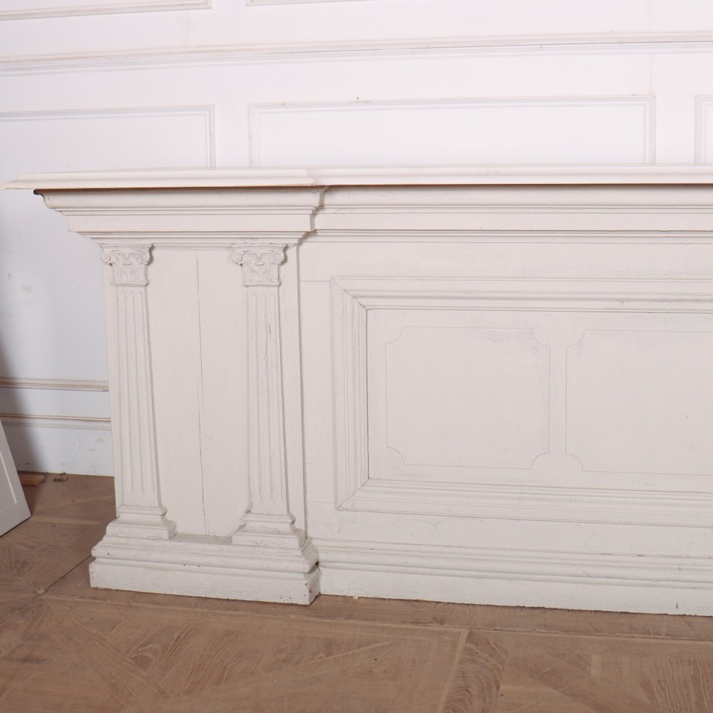 A long off-white painted timber shop counter featuring fluted Corinthian pilasters and recessed panel moulding along the front. View V