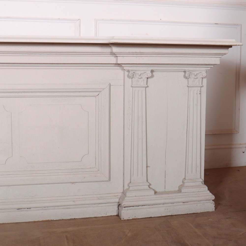 A long off-white painted timber shop counter featuring fluted Corinthian pilasters and recessed panel moulding along the front. View VI
