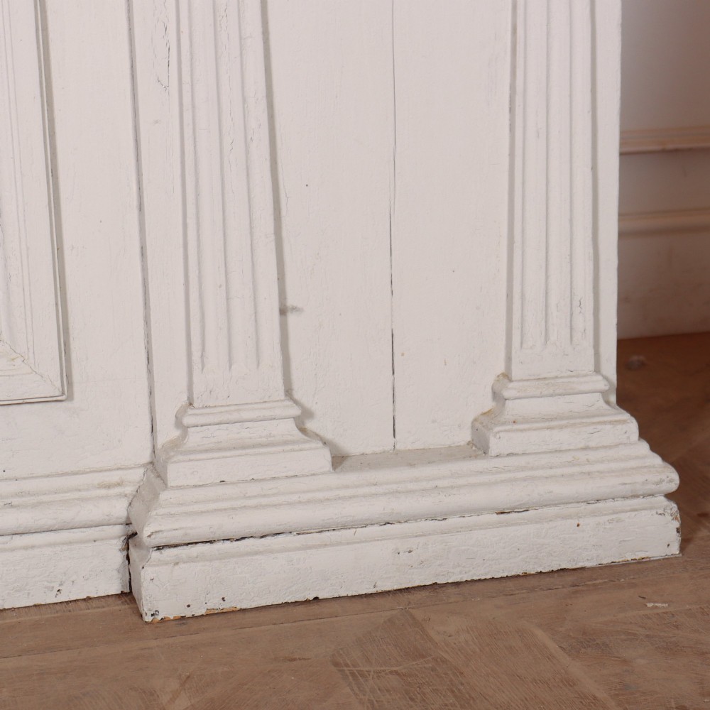 A long off-white painted timber shop counter featuring fluted Corinthian pilasters and recessed panel moulding along the front. View VIII
