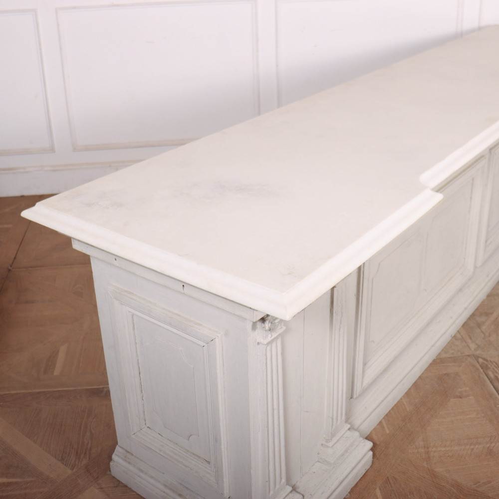 A long off-white painted timber shop counter featuring fluted Corinthian pilasters and recessed panel moulding along the front. View X