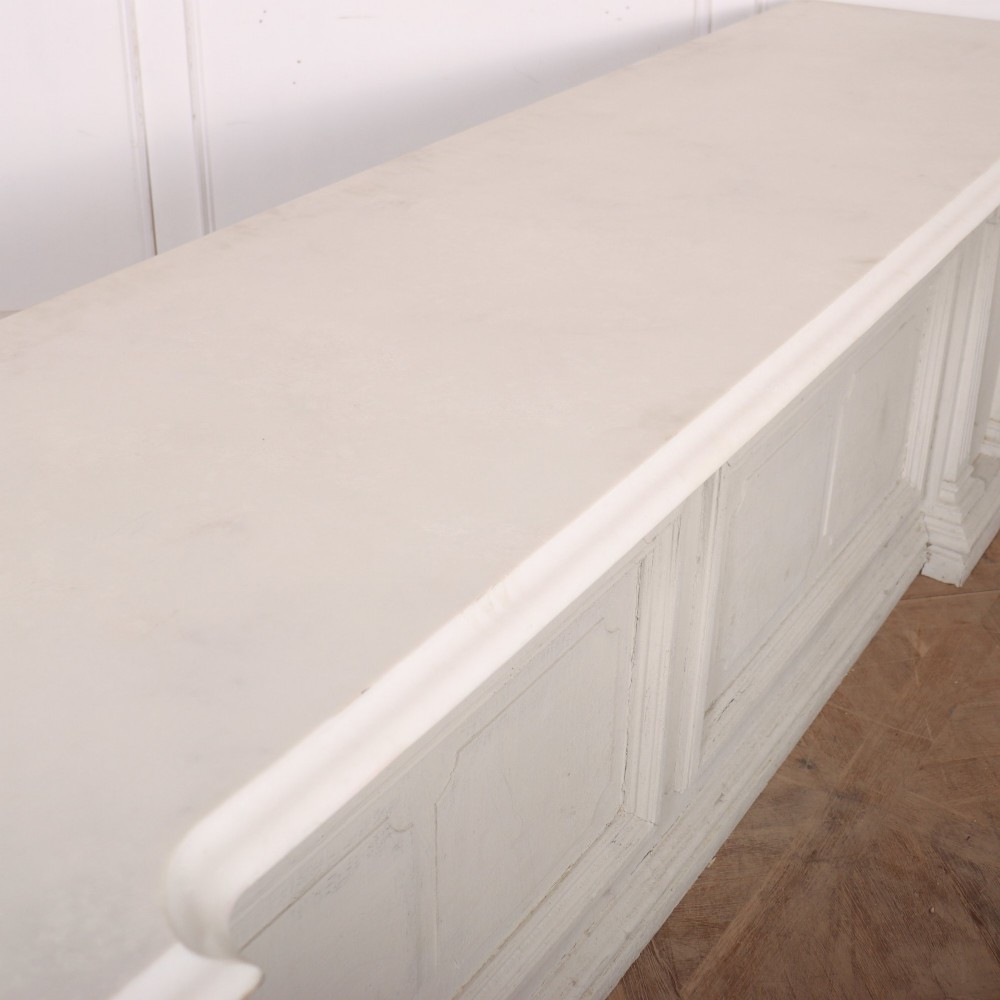 A long off-white painted timber shop counter featuring fluted Corinthian pilasters and recessed panel moulding along the front. View XI