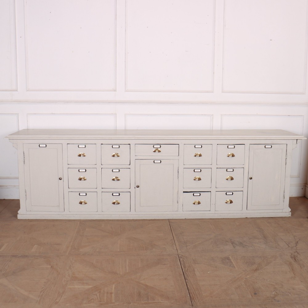 A long off-white painted timber shop counter featuring fluted Corinthian pilasters and recessed panel moulding along the front. View XII