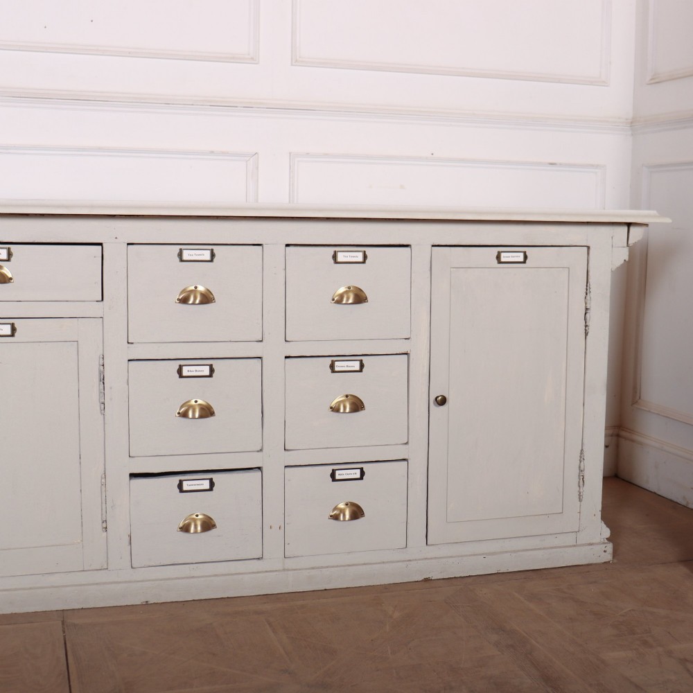 A long off-white painted timber shop counter featuring fluted Corinthian pilasters and recessed panel moulding along the front. View XIV