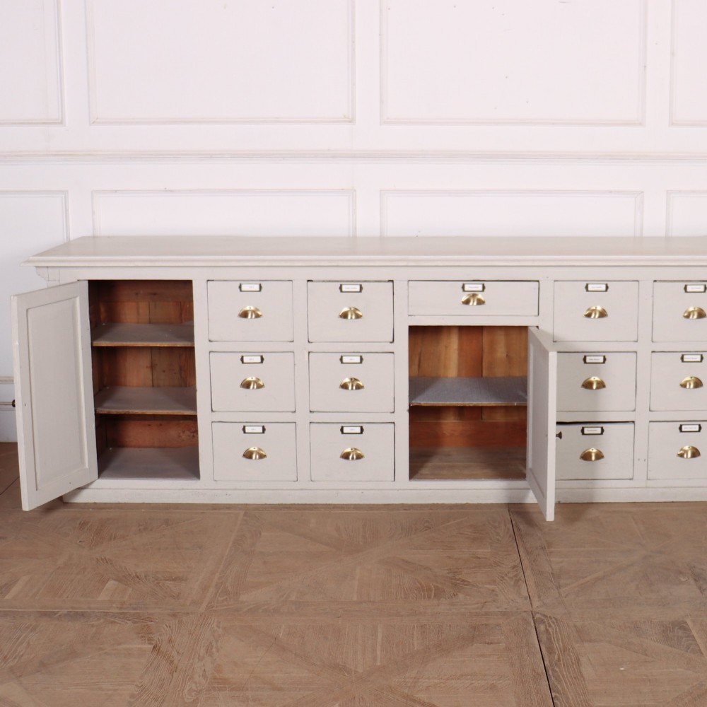 A long off-white painted timber shop counter featuring fluted Corinthian pilasters and recessed panel moulding along the front. View XV