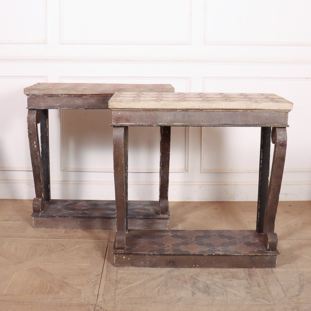 A pair of narrow Spanish painted wood console tables with curved upright supports, patterned top surfaces, and lower shelves.