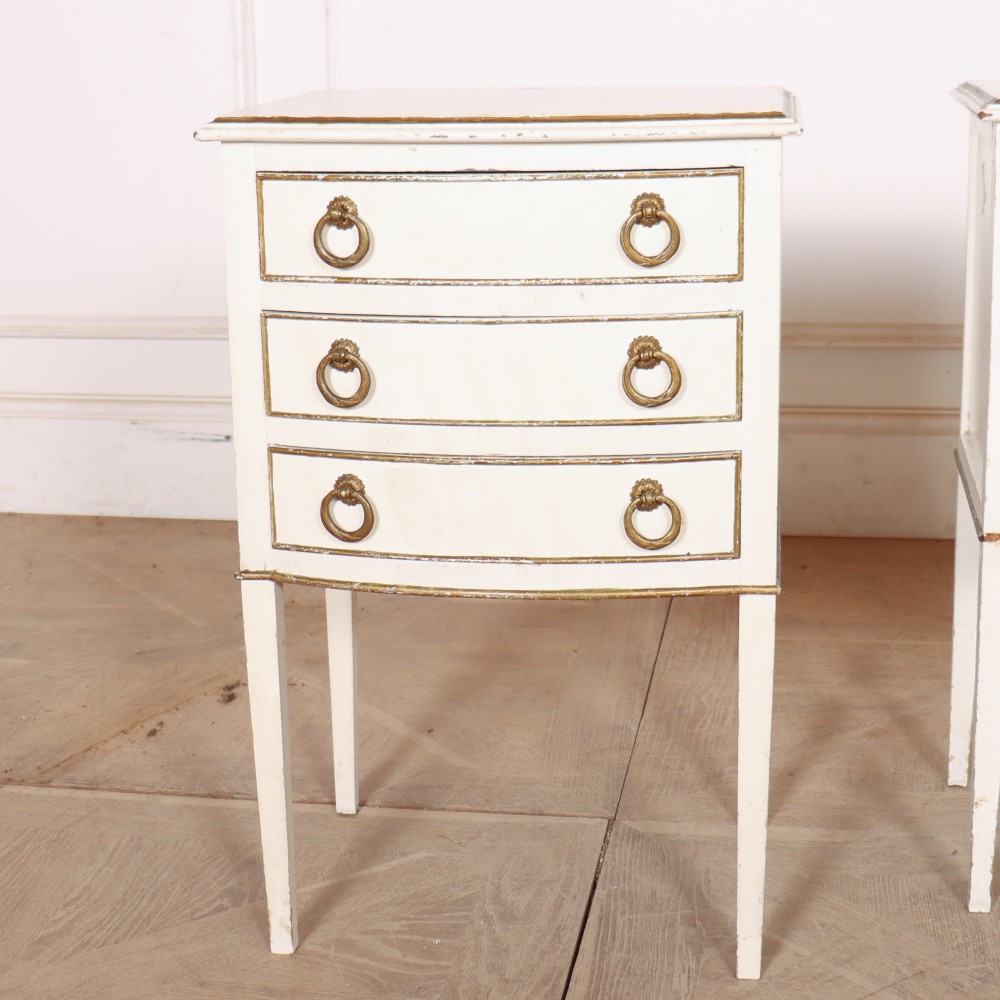 A pair of off-white painted French bedside chests featuring three curved drawers, gilded moulding details, brass ring handles, and tall square tapered legs. View II