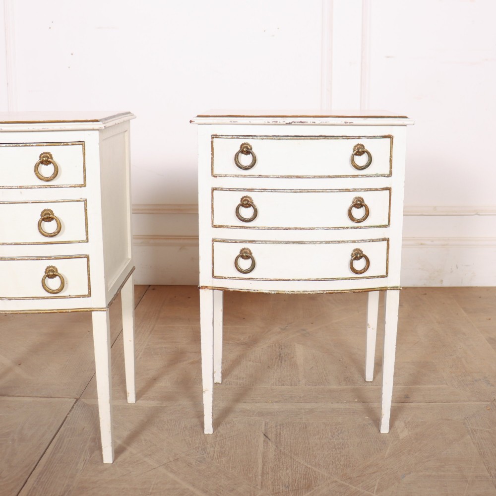 A pair of off-white painted French bedside chests featuring three curved drawers, gilded moulding details, brass ring handles, and tall square tapered legs. View III