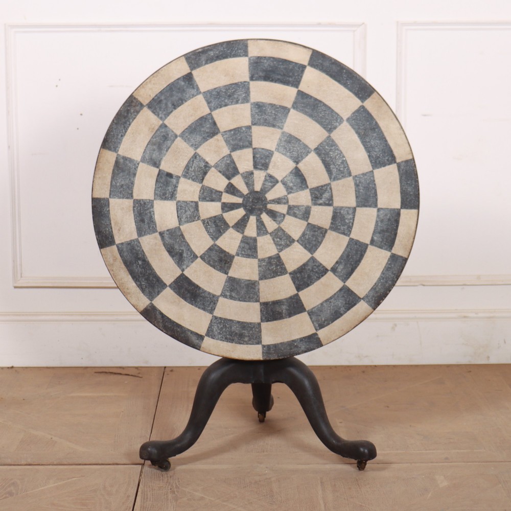 A circular tilt-top tripod table featuring a painted concentric checkerboard top in black and cream, supported by a dark three-legged base on castors.