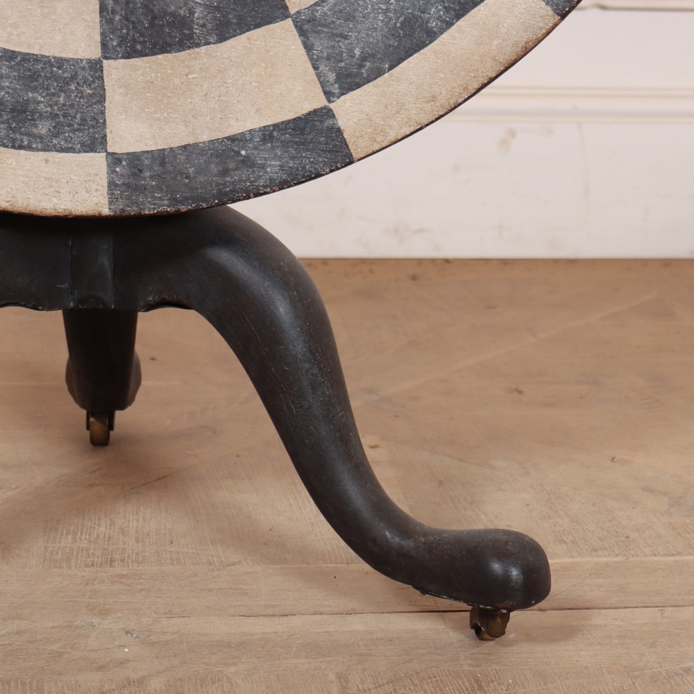 A circular tilt-top tripod table featuring a painted concentric checkerboard top in black and cream, supported by a dark three-legged base on castors. View III