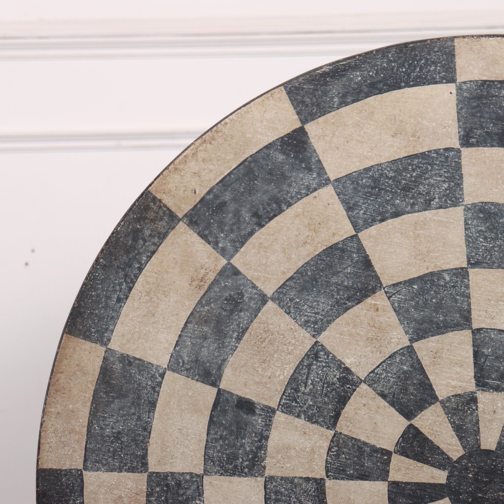 A circular tilt-top tripod table featuring a painted concentric checkerboard top in black and cream, supported by a dark three-legged base on castors. View V