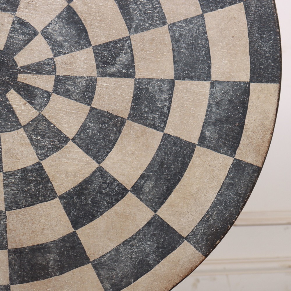 A circular tilt-top tripod table featuring a painted concentric checkerboard top in black and cream, supported by a dark three-legged base on castors. View VI