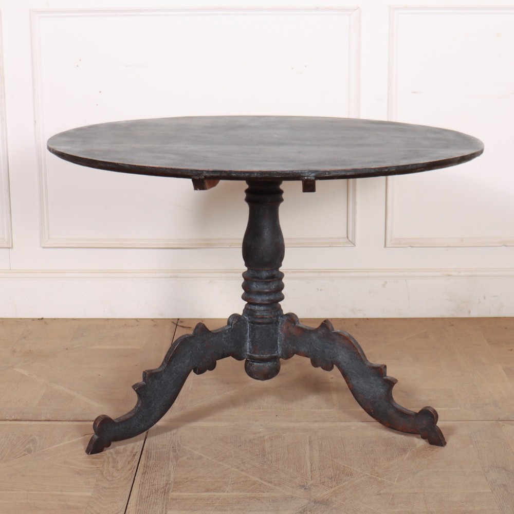 An antique Swedish round supper table featuring a dark distress-painted top set on a turned baluster pedestal with shaped tripod legs.