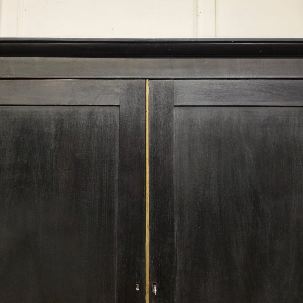 An ebonised black timber linen cupboard featuring two upper panelled doors above two short and two long drawers with brass drop handles. View VII