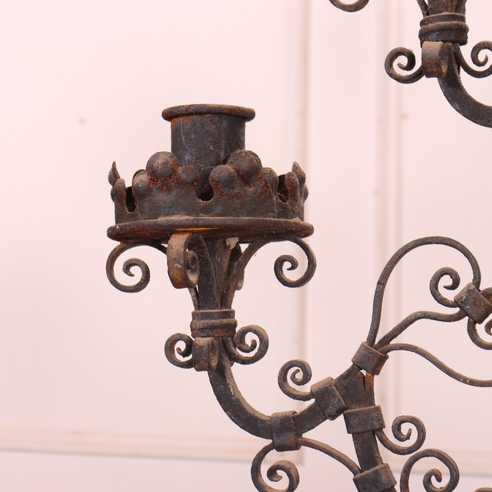 A tall dark wrought iron floor candelabra featuring scrollwork arms holding six candle sconces above a decorated stem and tripod scroll base. View V