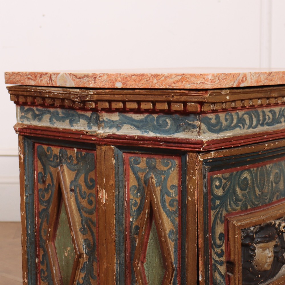 An antique Italian polychrome painted cabinet with a pink marble top, canted corners, and a central carved face mask panel. View VII