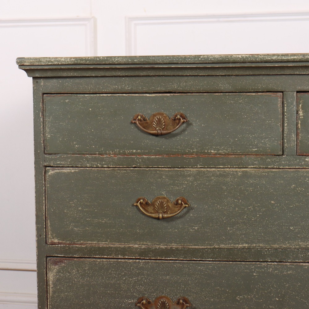 A distressed sage green painted wooden chest of drawers featuring two short over three long drawers with decorative brass handles and bracket feet. View II